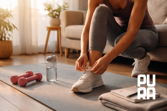 Mujer preparándose para entrenar en casa al amanecer, atándose las zapatillas junto a esterilla y mancuernas, representando la constancia en hábitos saludables y el progreso sostenible.