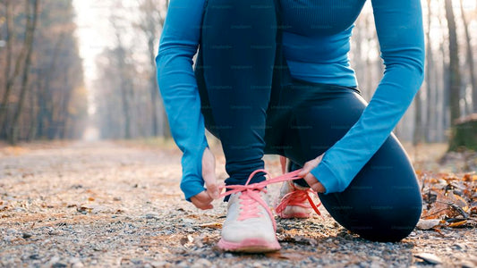 Mujer atándose las zapatillas antes de entrenar en un sendero, ejemplo de disciplina y progreso sostenible en fitness.